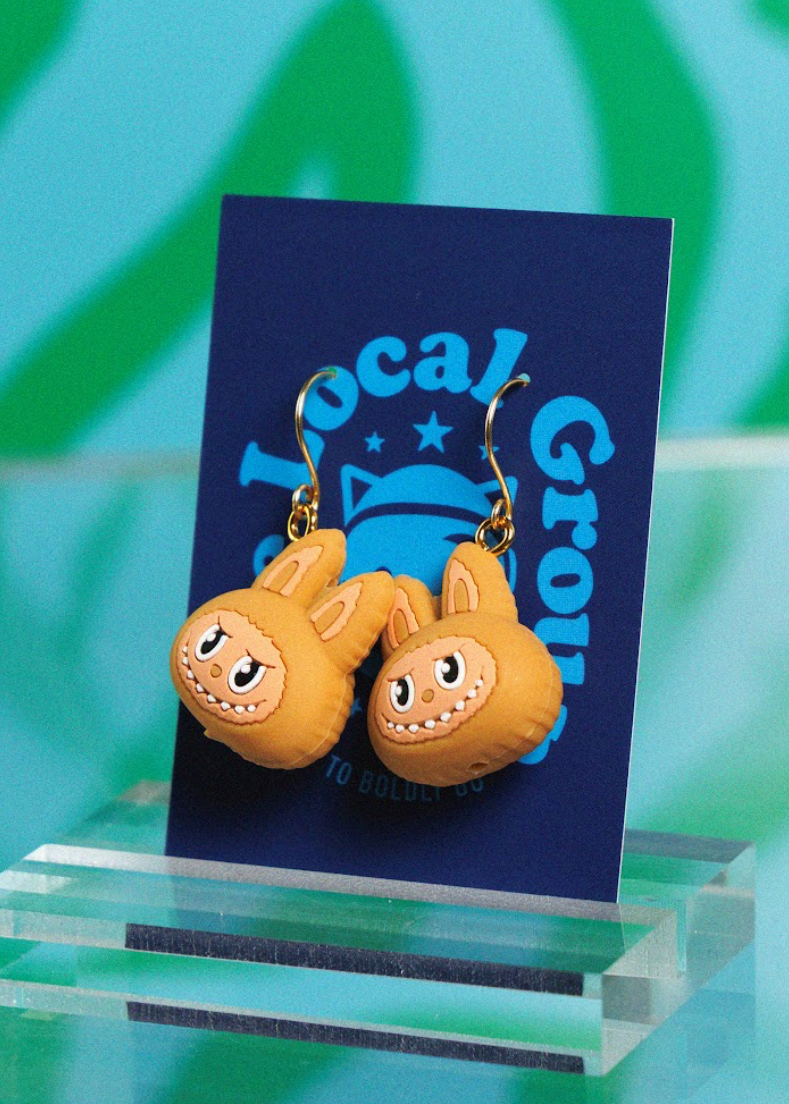 Pair of cartoonish orange earrings on a blue card with 'Local Group' branding.