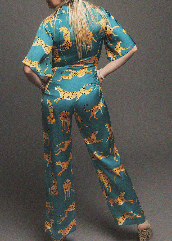 Woman wearing a teal jumpsuit with gold animal print on a gray background