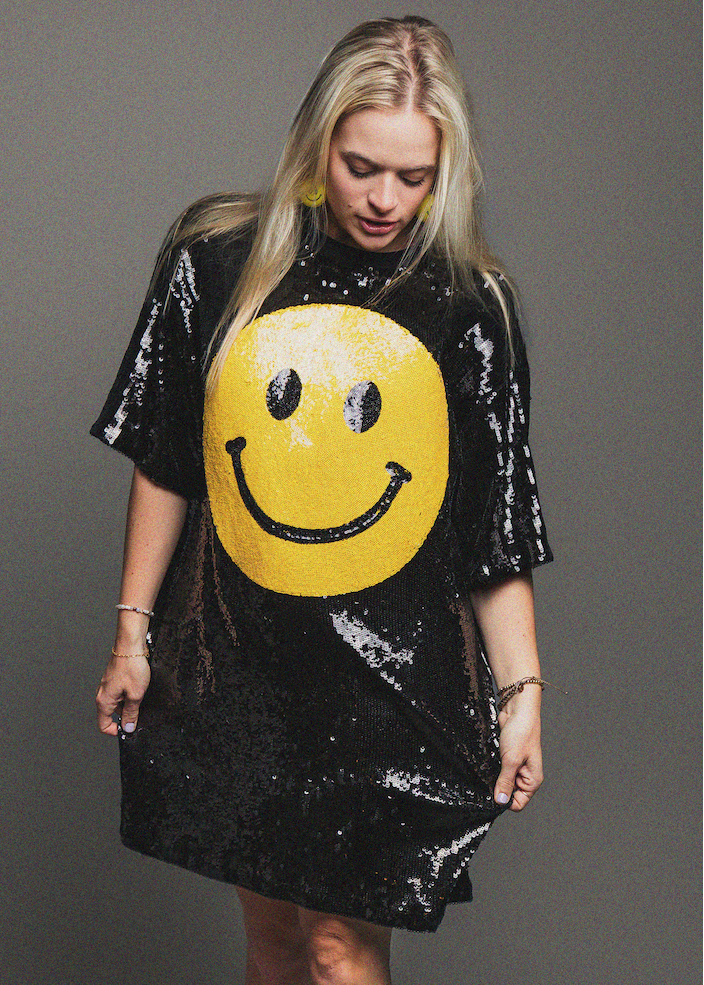 Person wearing a black sequin dress with a yellow smiley face design on a gray background