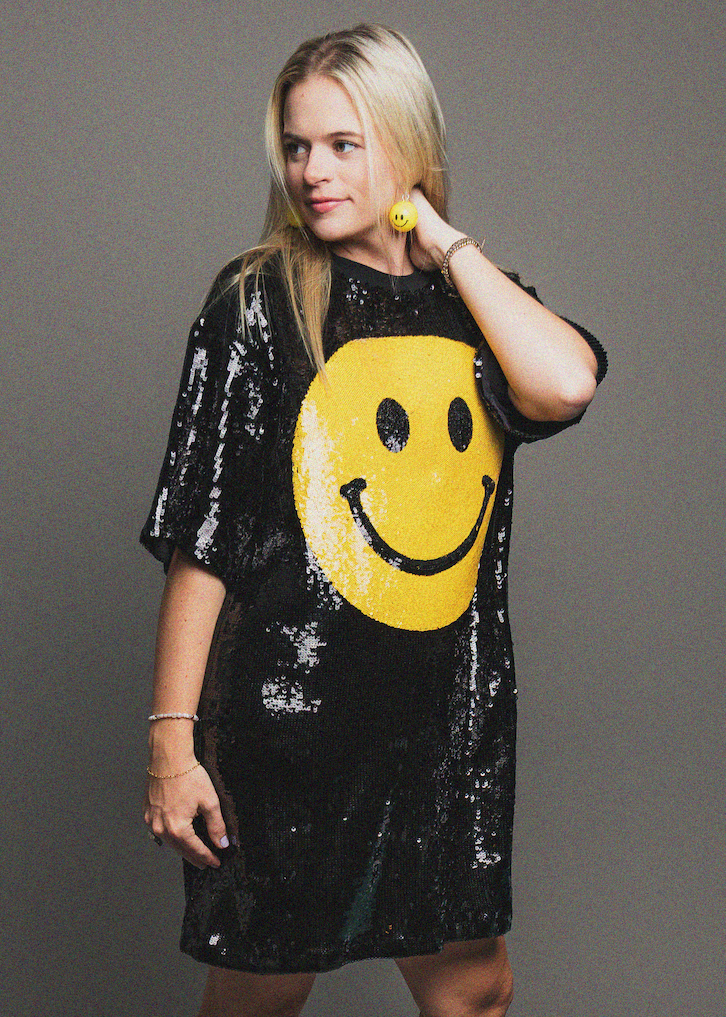 Woman wearing a black sequin dress with a yellow smiley face design on a gray background