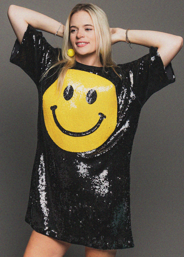 Person wearing a black sequin dress with a yellow smiley face design on a gray background