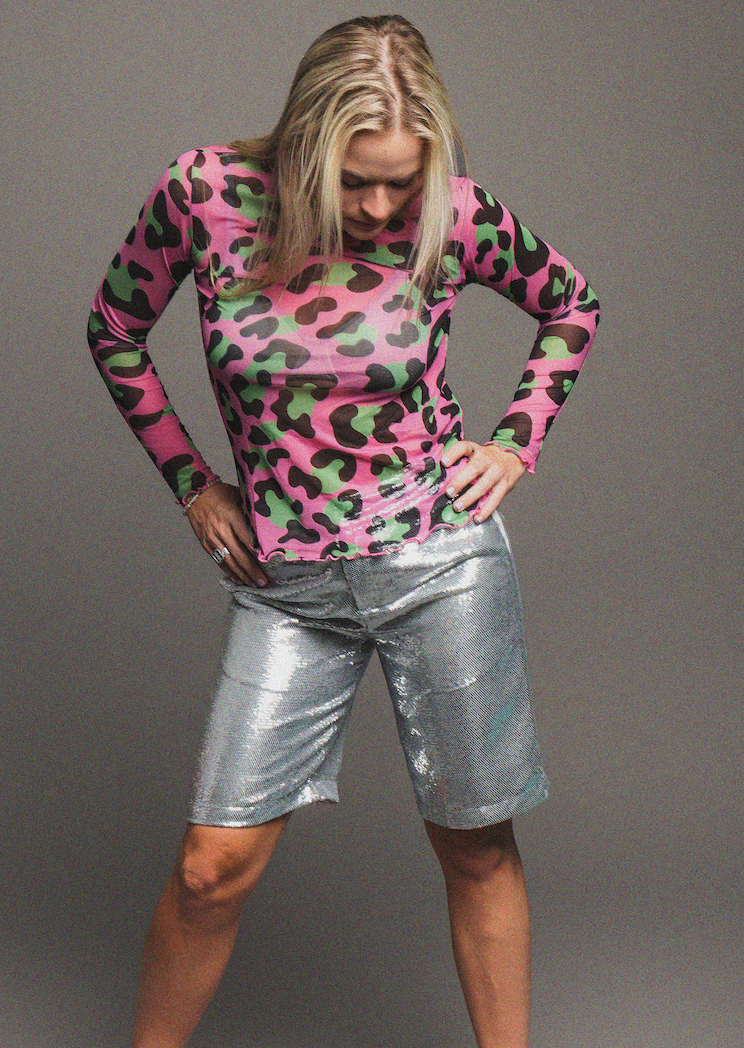 Person wearing a pink and green leopard print long-sleeve shirt and silver shorts on a gray background