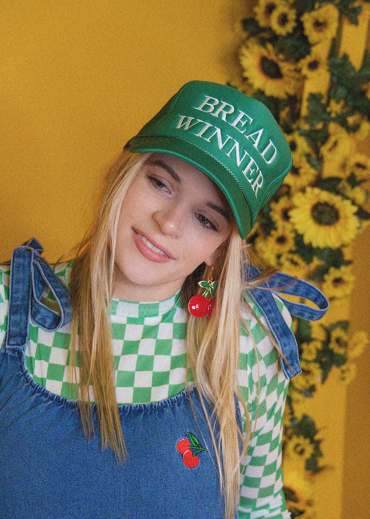 Person wearing a green 'Bread Winner' cap with a yellow floral background
