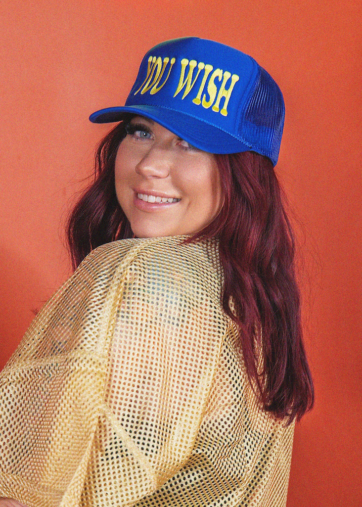 Woman wearing a blue cap with 'YOU WISH' text against a red background