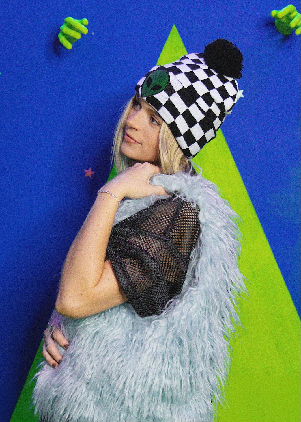 Person wearing a checkered hat and fluffy vest against a colorful background