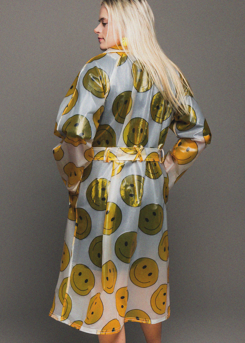 Woman wearing a rain coat with smiley face pattern on a gray background