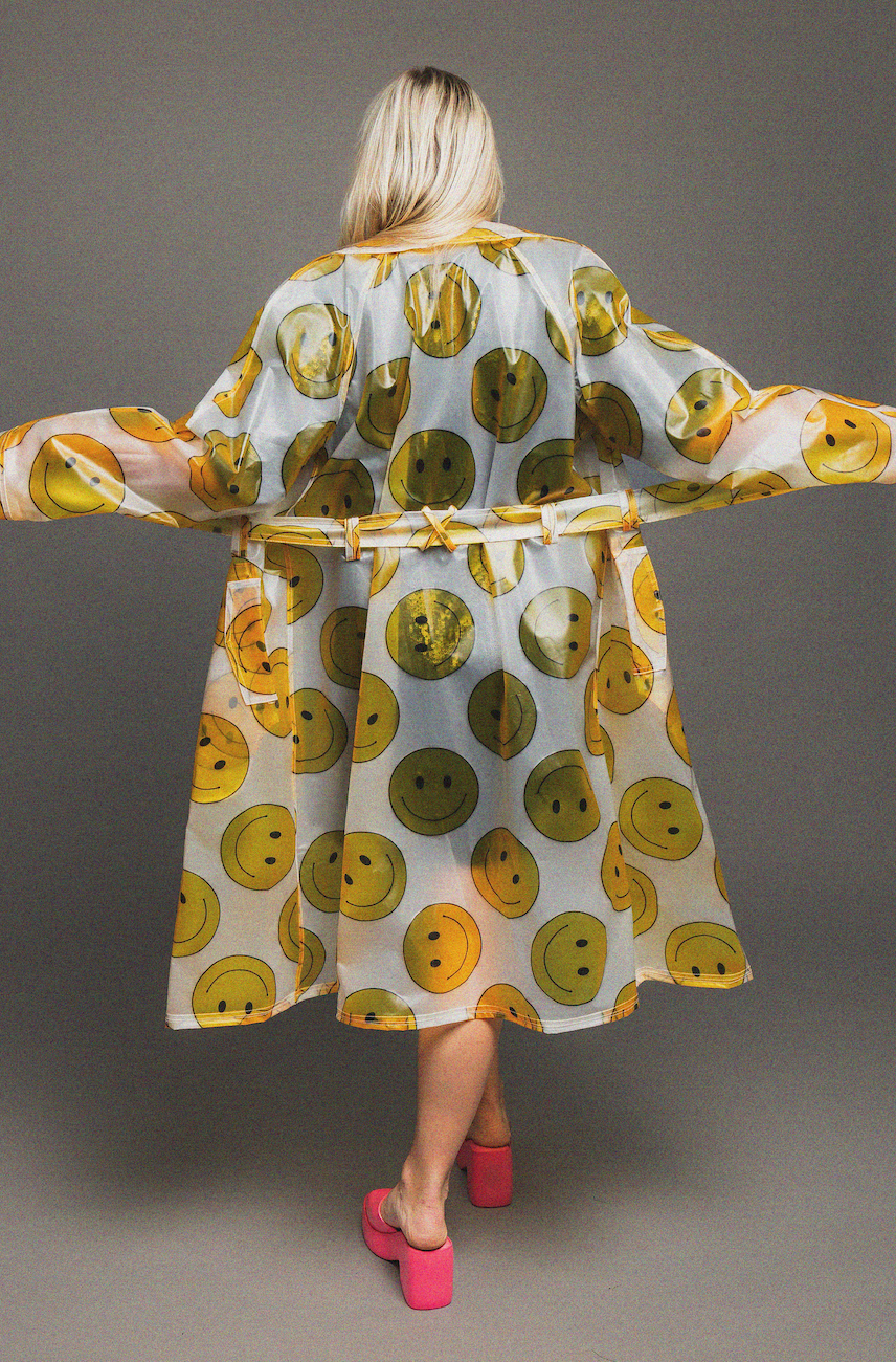 Woman wearing a rain coat with smiley face pattern on a gray background