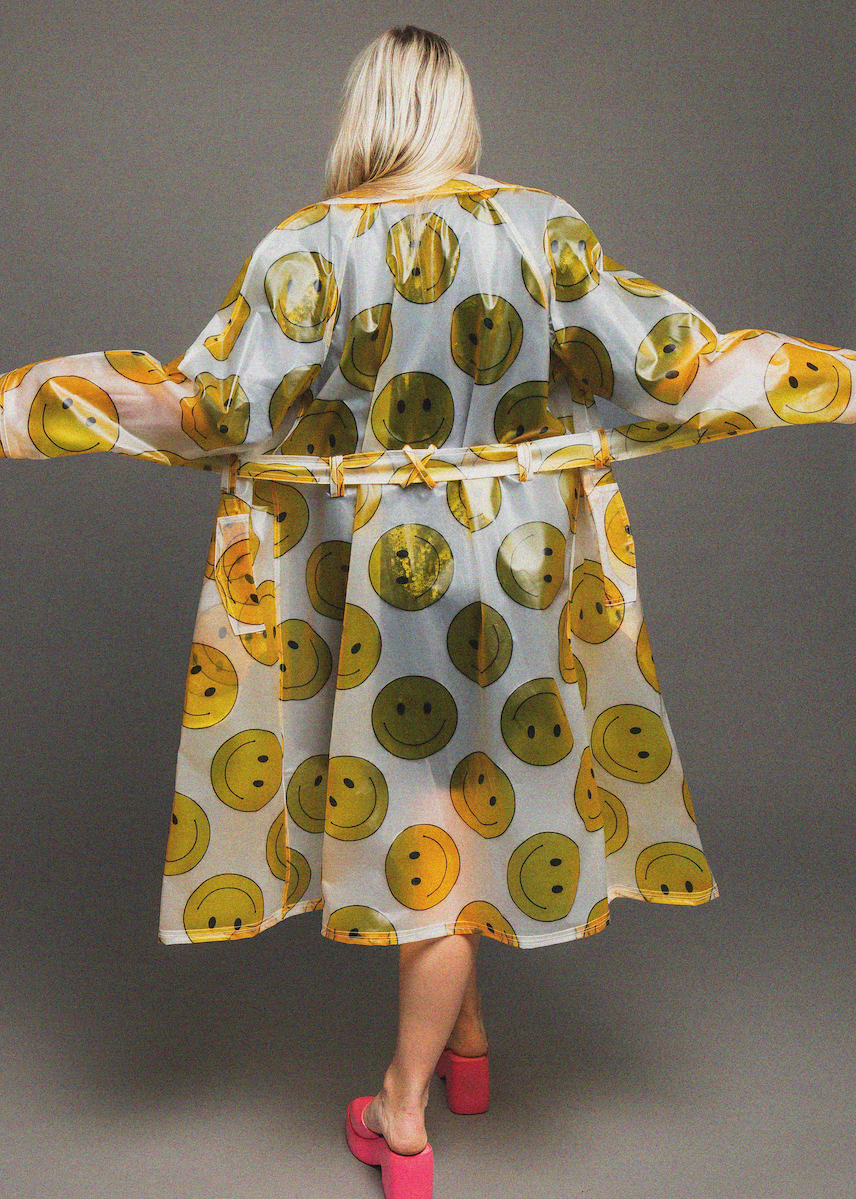 Woman wearing a rain coat with smiley face pattern on a gray background