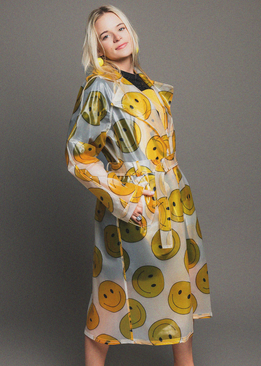 Woman wearing a rain coat with smiley face pattern on a gray background
