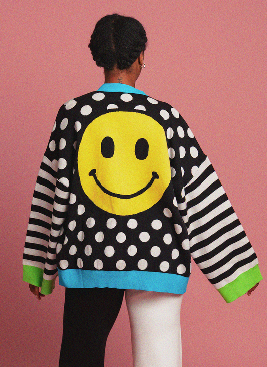 Person wearing a polka dot cardigan with smiley face designs on a pink background