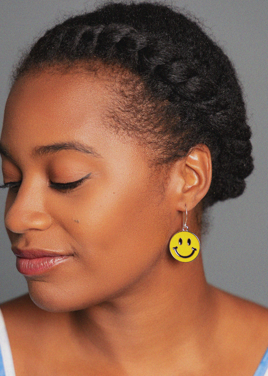 Woman wearing a yellow smiley face earring against a gray background