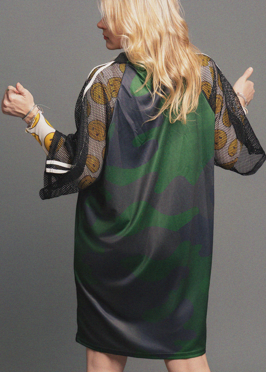 Woman wearing a green and black patterned dress with sheer sleeves against a gray background