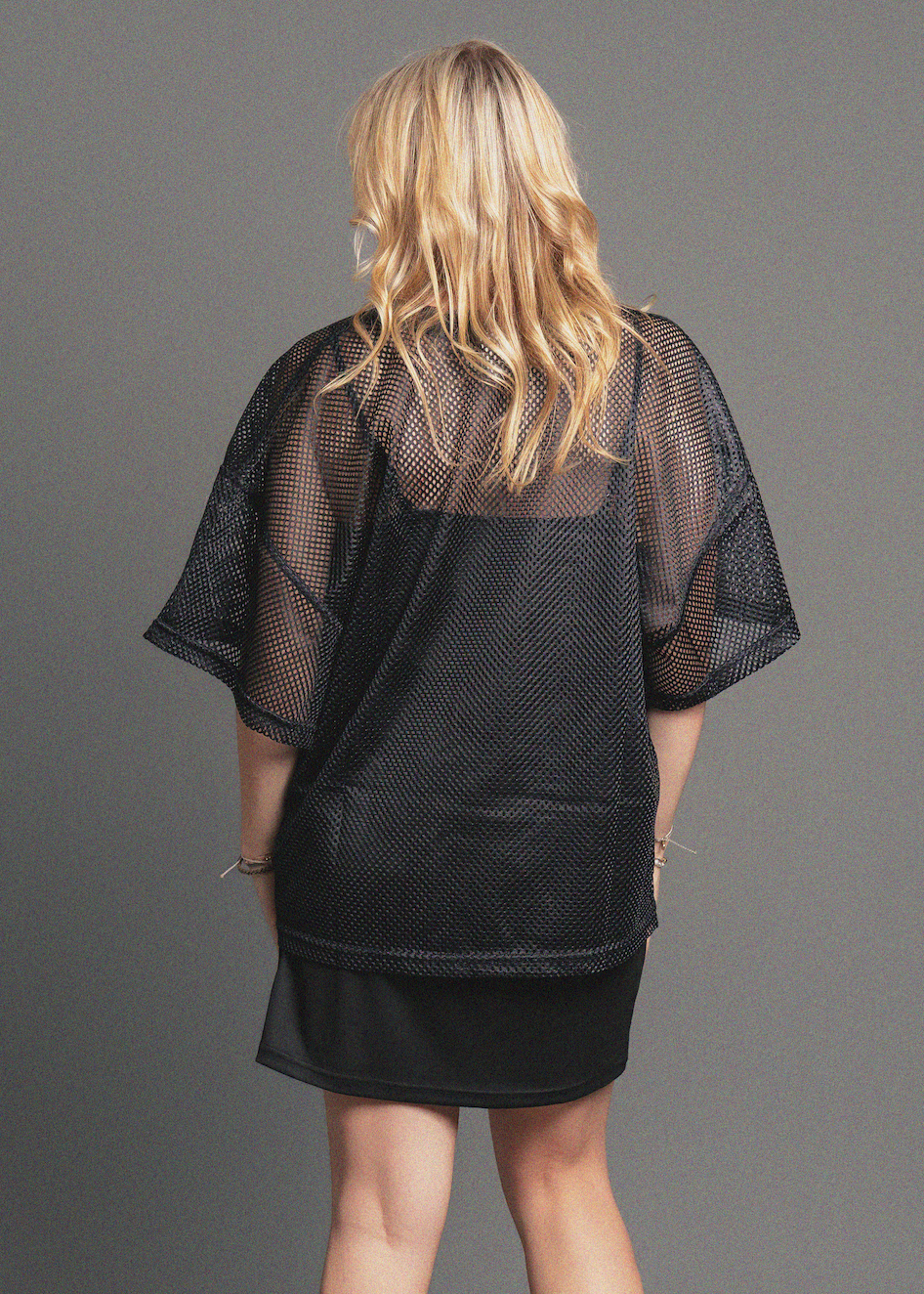 Person wearing a black mesh cover-up against a gray background