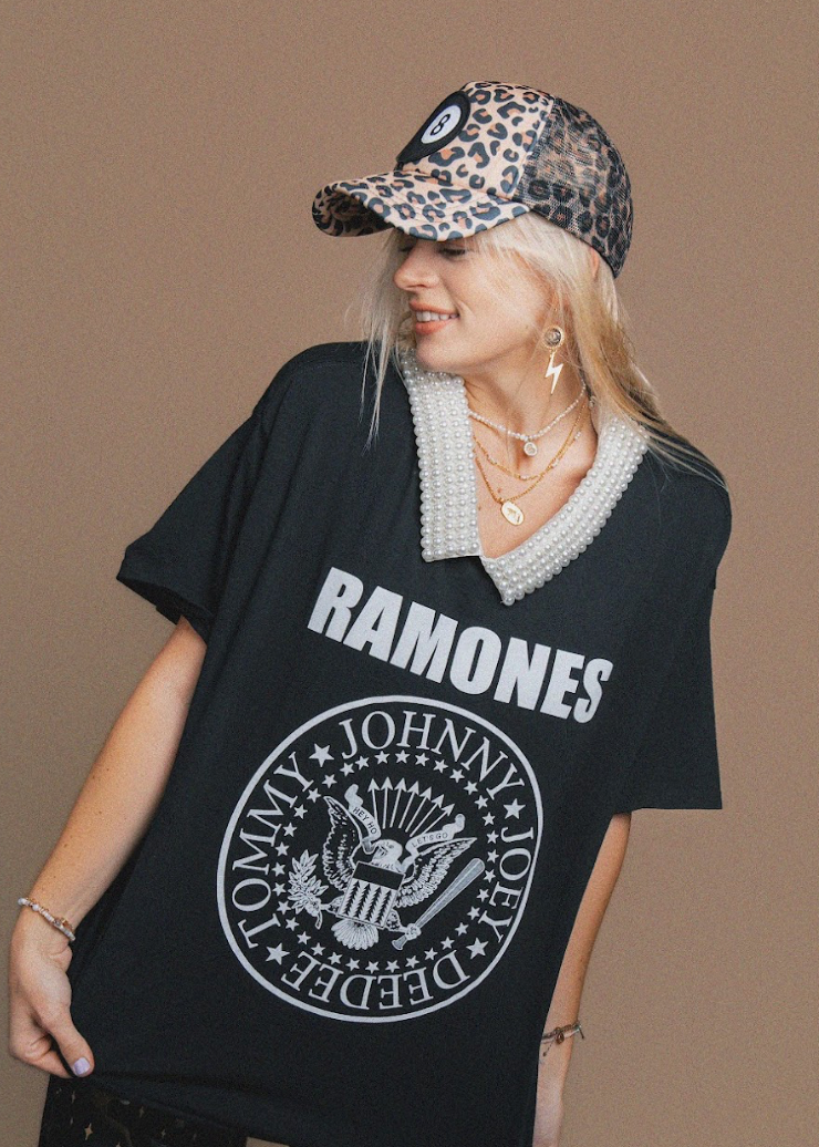 Person wearing a black 'RAMONES' t-shirt with a leopard print cap on a brown background