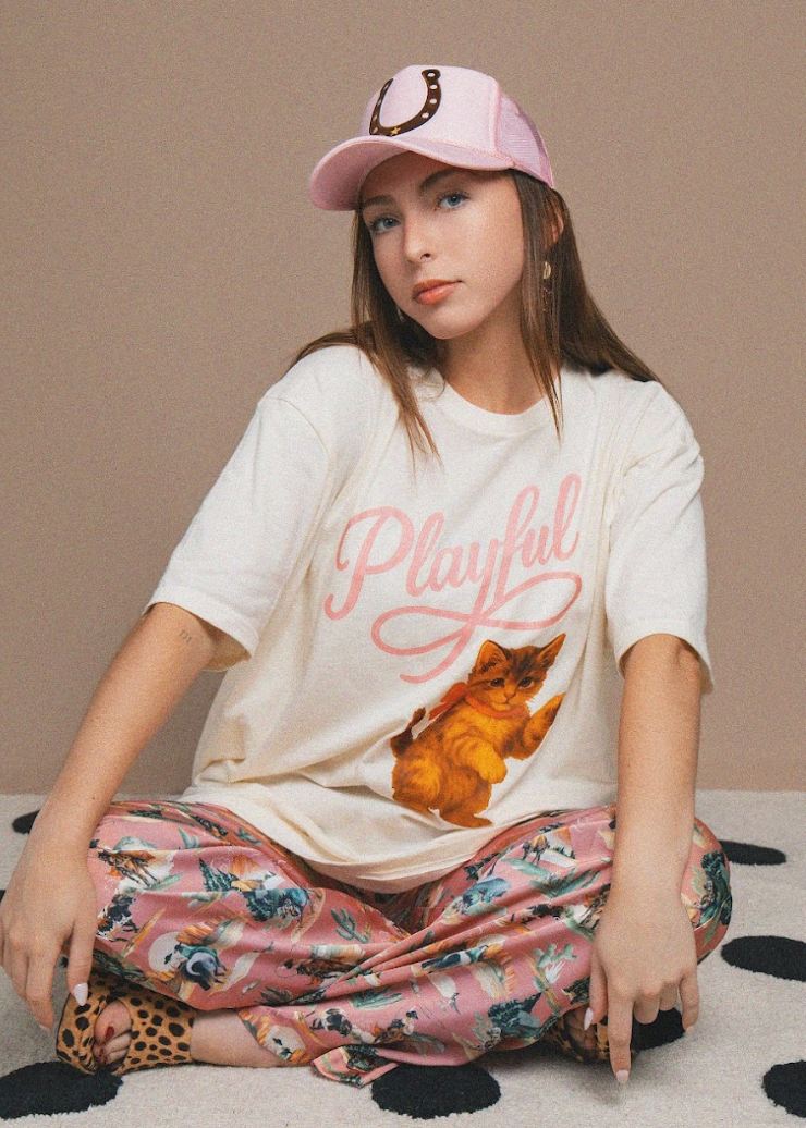 Person wearing a white t-shirt with a graphic and text, sitting on a patterned surface.
