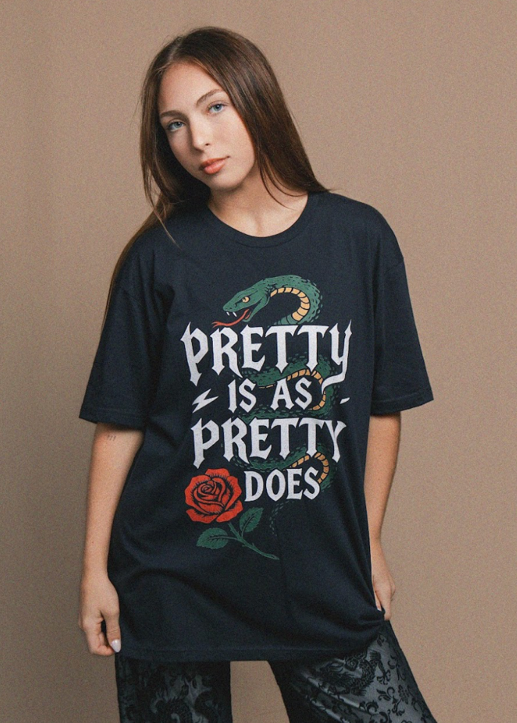 Person wearing a black t-shirt with a snake and rose design and text on a beige background