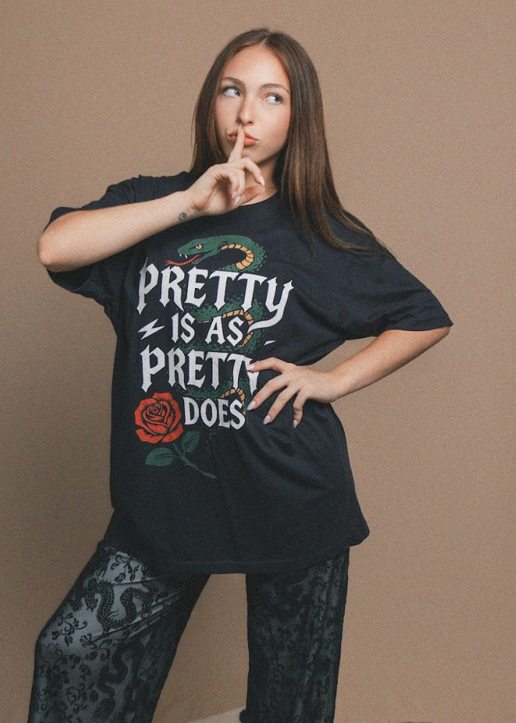 Person wearing a black t-shirt with a graphic design and text, posing against a brown background