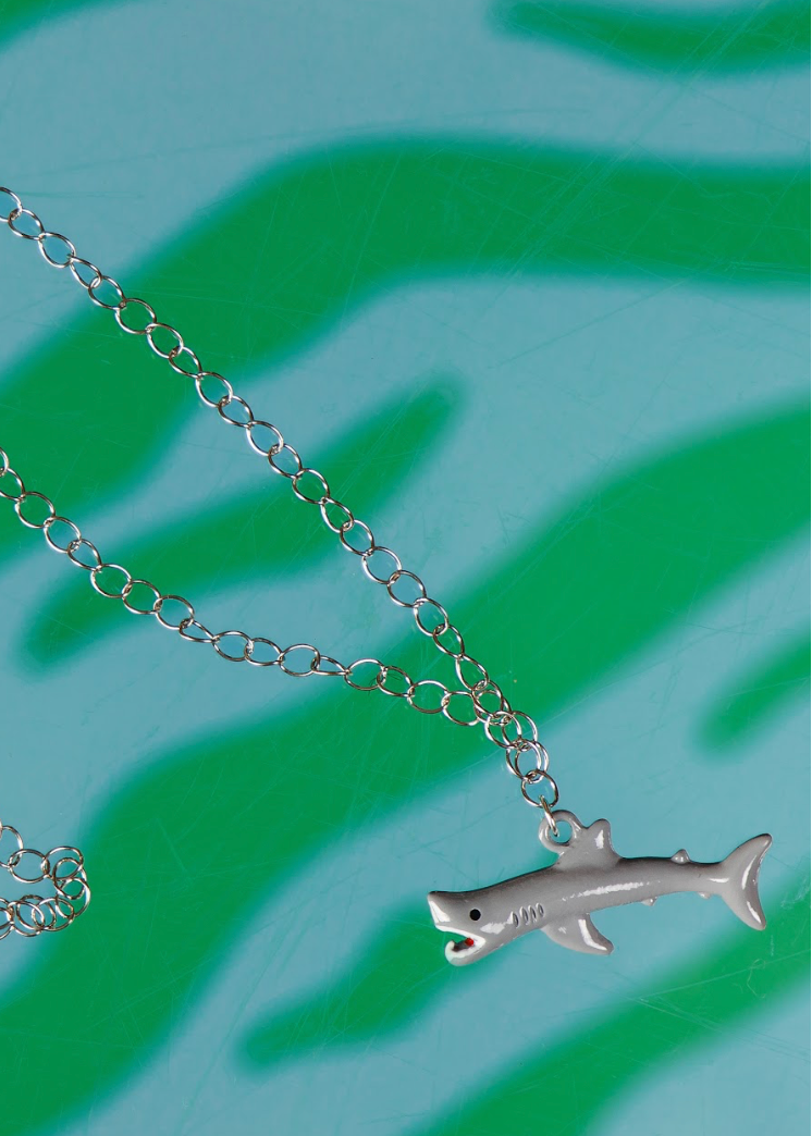 Silver shark pendant necklace on a green background
