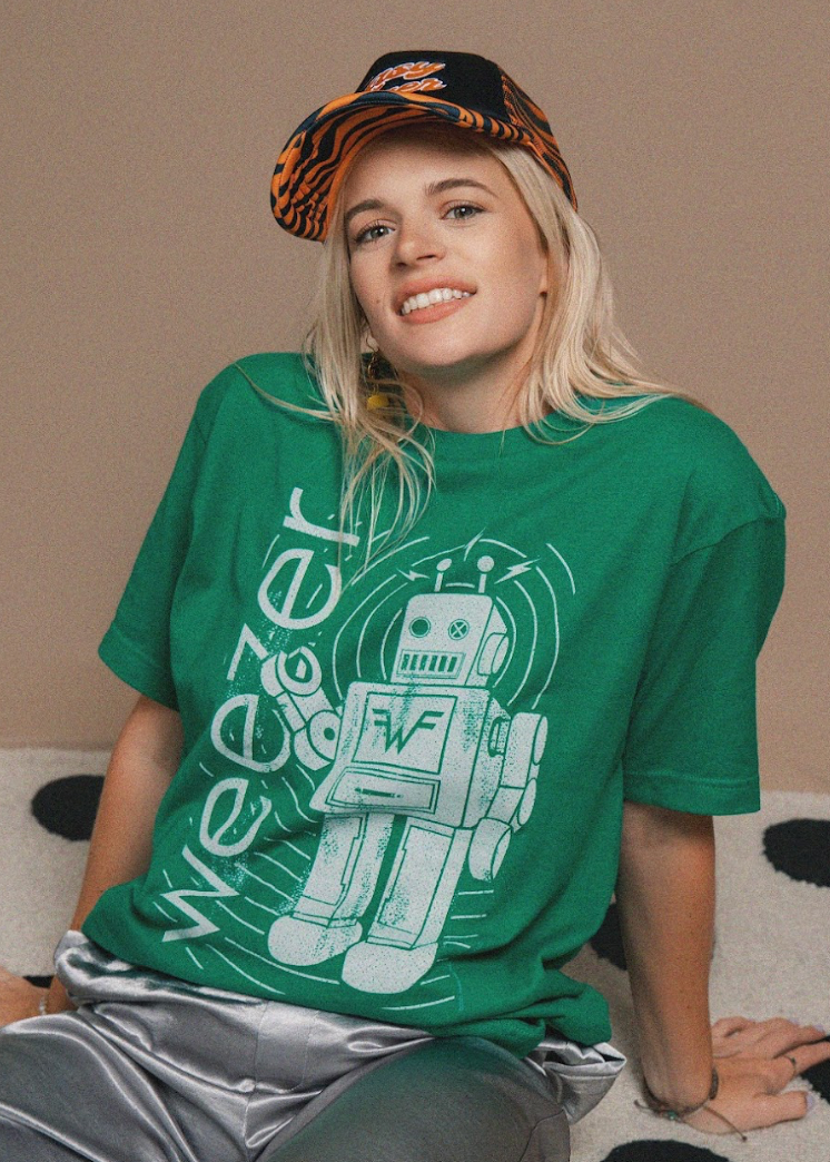 Person wearing a green t-shirt with a robot graphic and 'Weezer' text, sitting on a carpeted floor.