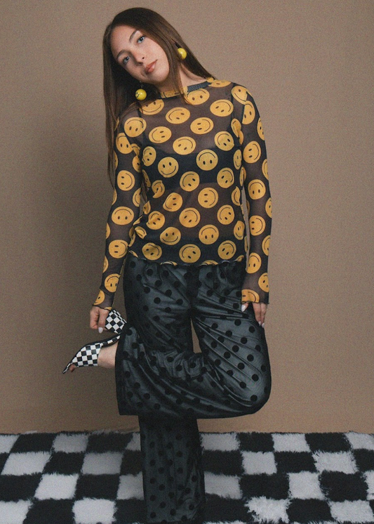 Woman wearing a black outfit with yellow smiley face patterns on a checkered floor.