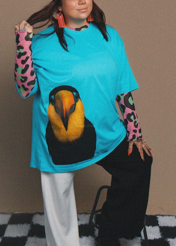 Person wearing a blue t-shirt with a toucan design on a checkered floor.