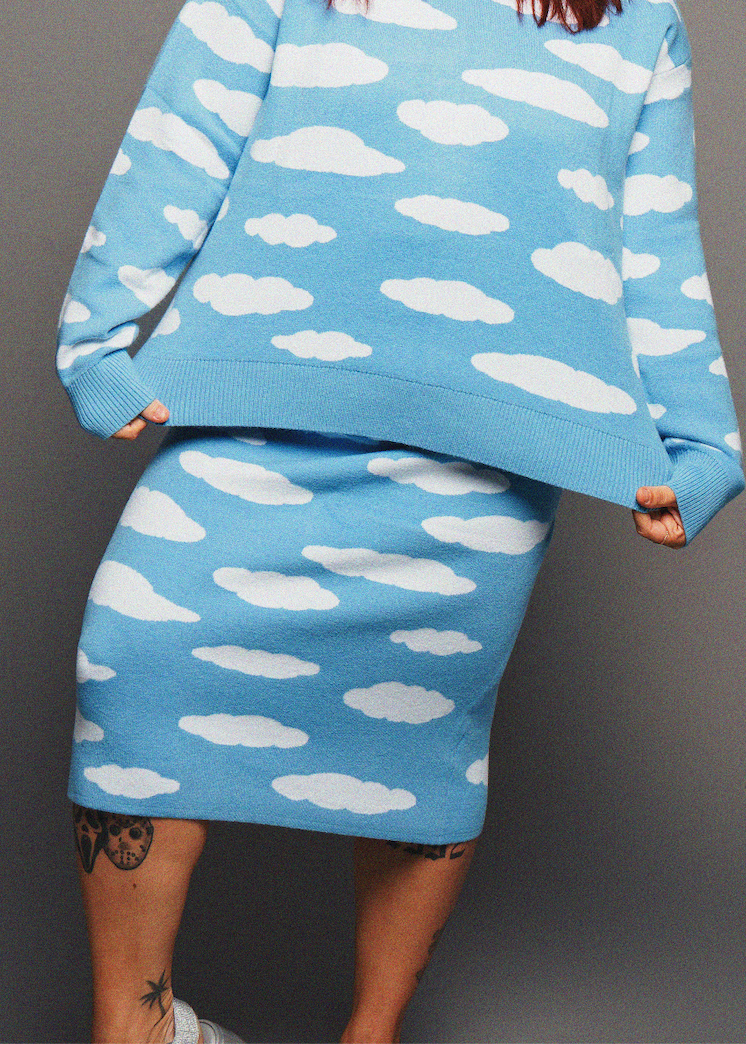 Person wearing a blue sweater and skirt with white cloud patterns on a gray background
