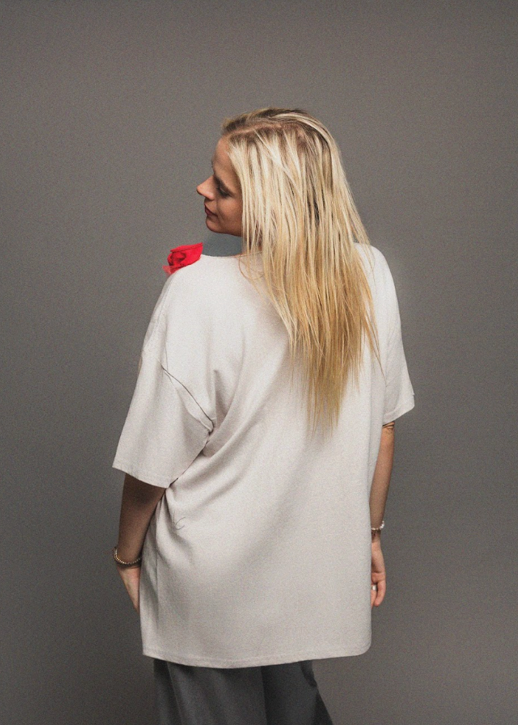 Woman wearing a light gray oversized shirt with a red flower detail on a plain background