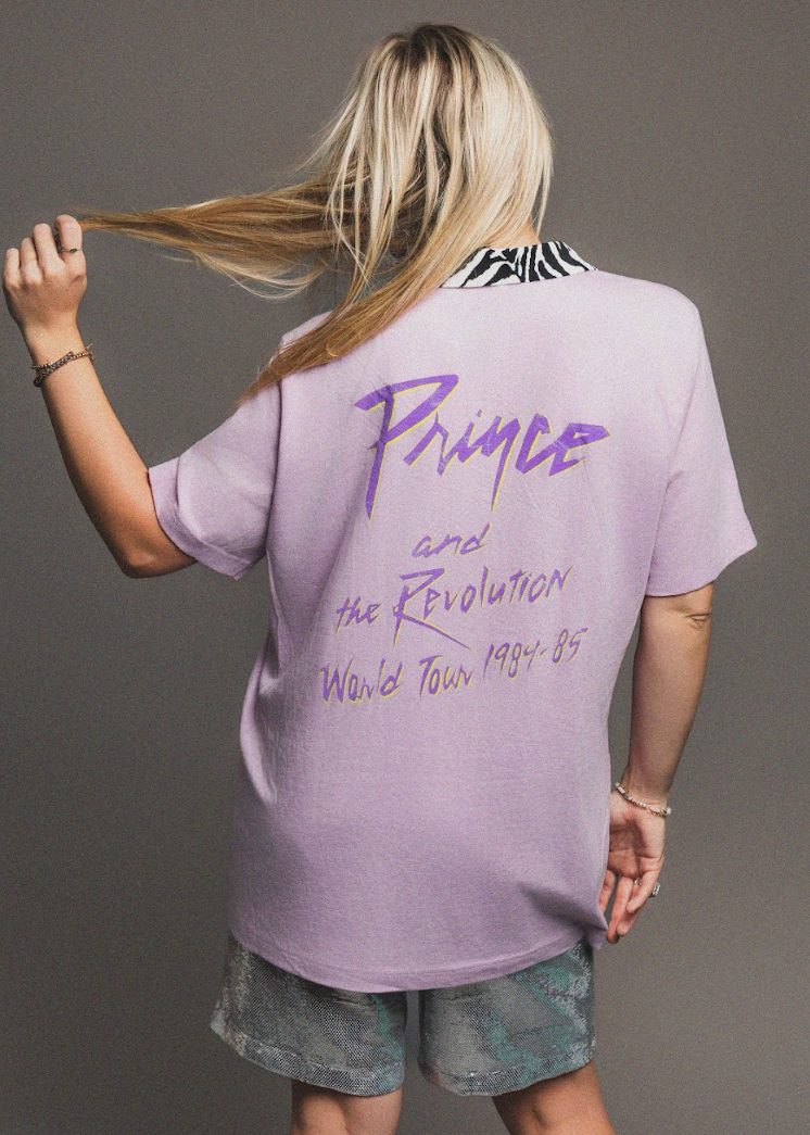 Person wearing a purple 'Prince' t-shirt with text on the back against a gray background