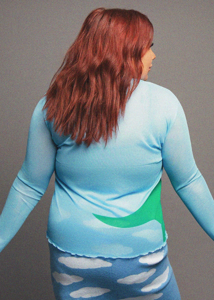 Person wearing a blue and green long-sleeve top with a blue skirt with cloud pattern on gray background