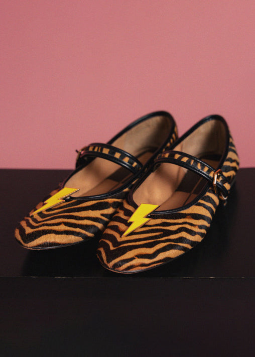 Pair of zebra-striped shoes with yellow bolt clip ons on a dark surface and pink background