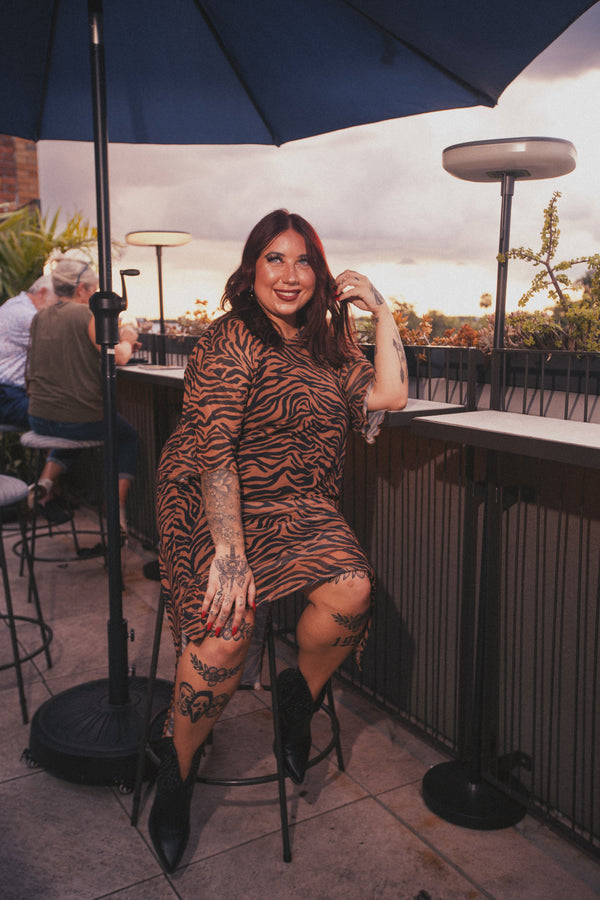 Woman in a tiger print dress sitting under an umbrella on a patio.
