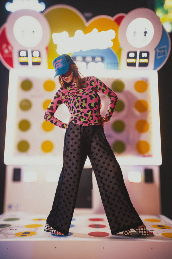 Person wearing a colorful top and polka dot pants standing on a game board with a colorful backdrop