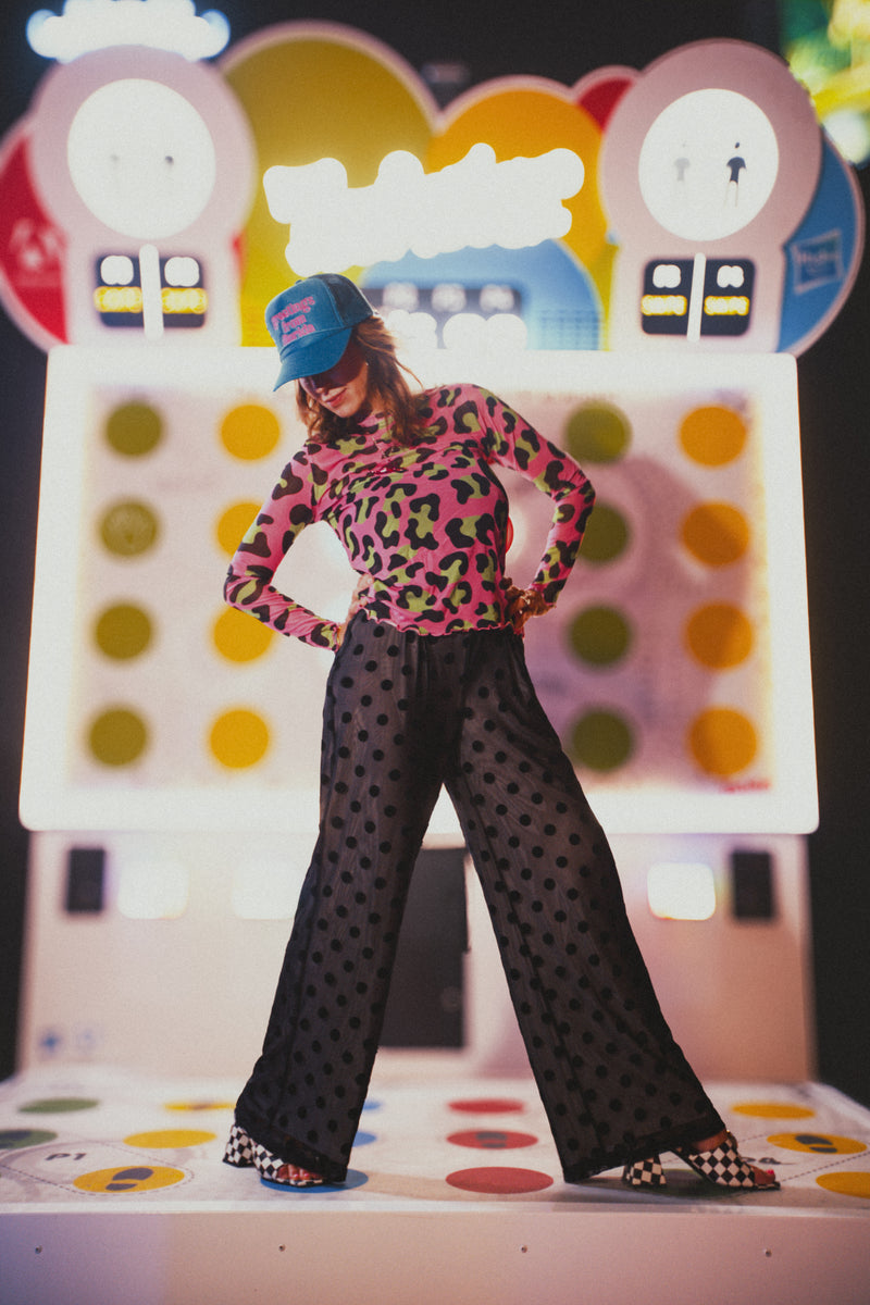 Person wearing a colorful top and polka dot pants standing on a game board with a colorful backdrop
