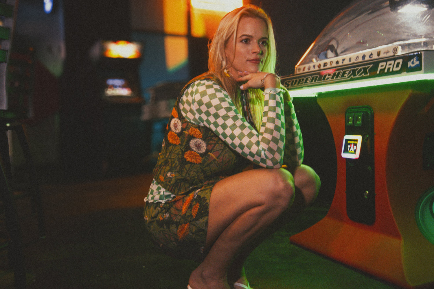 Woman sitting on a vintage arcade machine in a dimly lit room