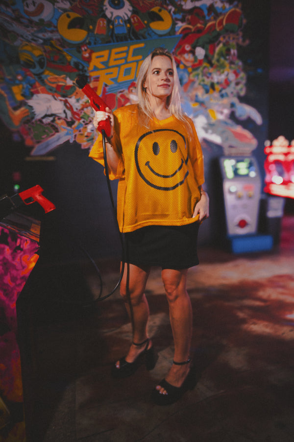 Person wearing a yellow smiley face shirt in an arcade setting