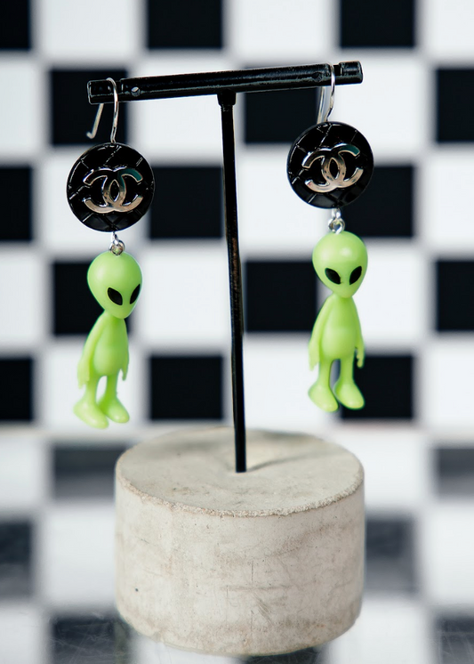 Green alien earrings with black CC logos on a checkered background