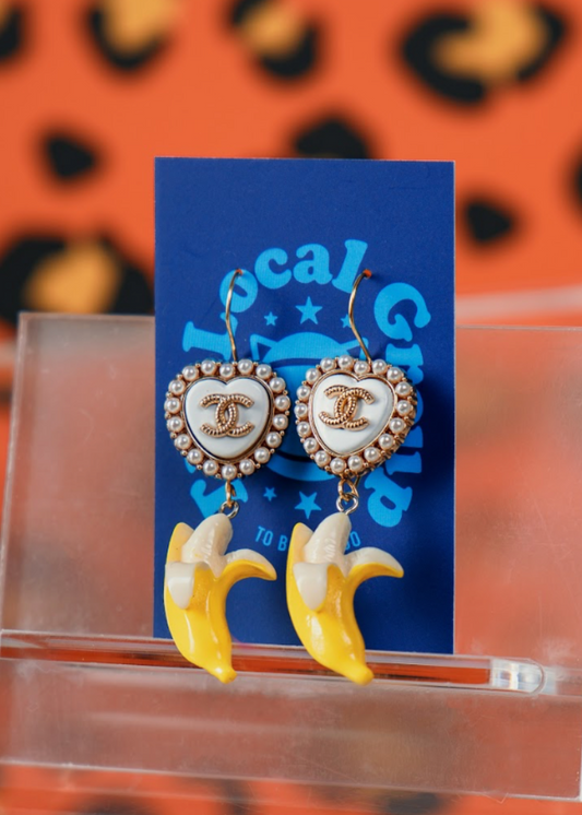 Heart-shaped earrings with banana designs on a clear stand against a leopard print background.