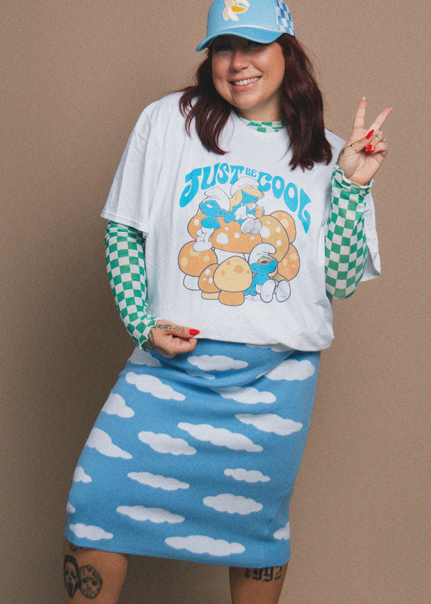 Person wearing a graphic t-shirt and cloud-patterned skirt with a plain background