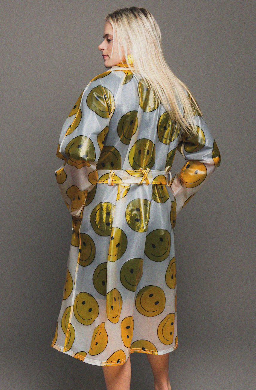 Woman wearing a rain coat with smiley face pattern on a gray background