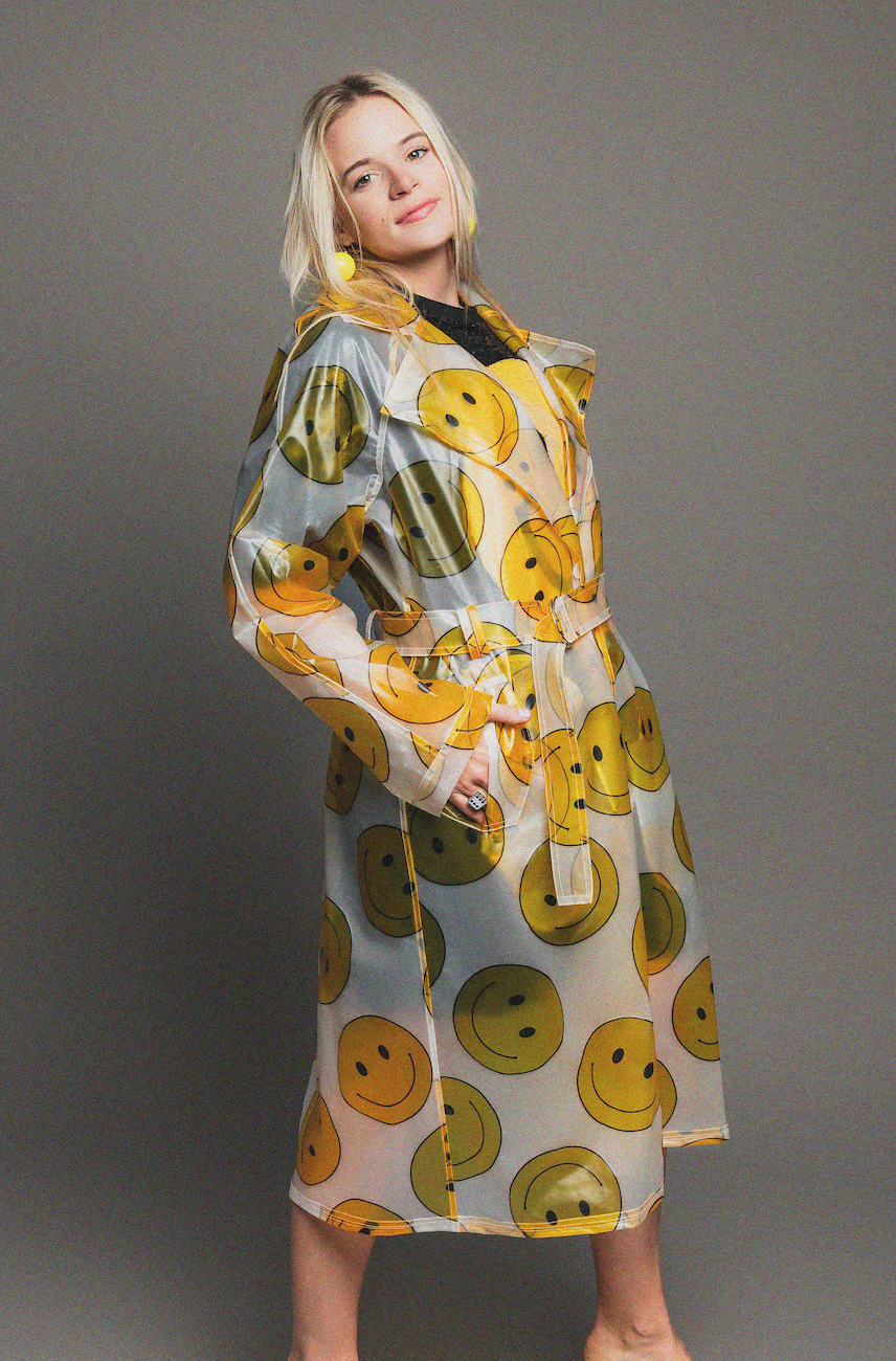 Woman wearing a rain coat with smiley face pattern on a gray background