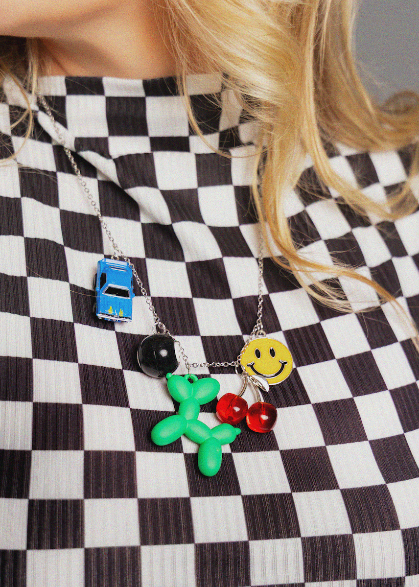 Person wearing a black and white checkered dress with colorful pendant necklaces.