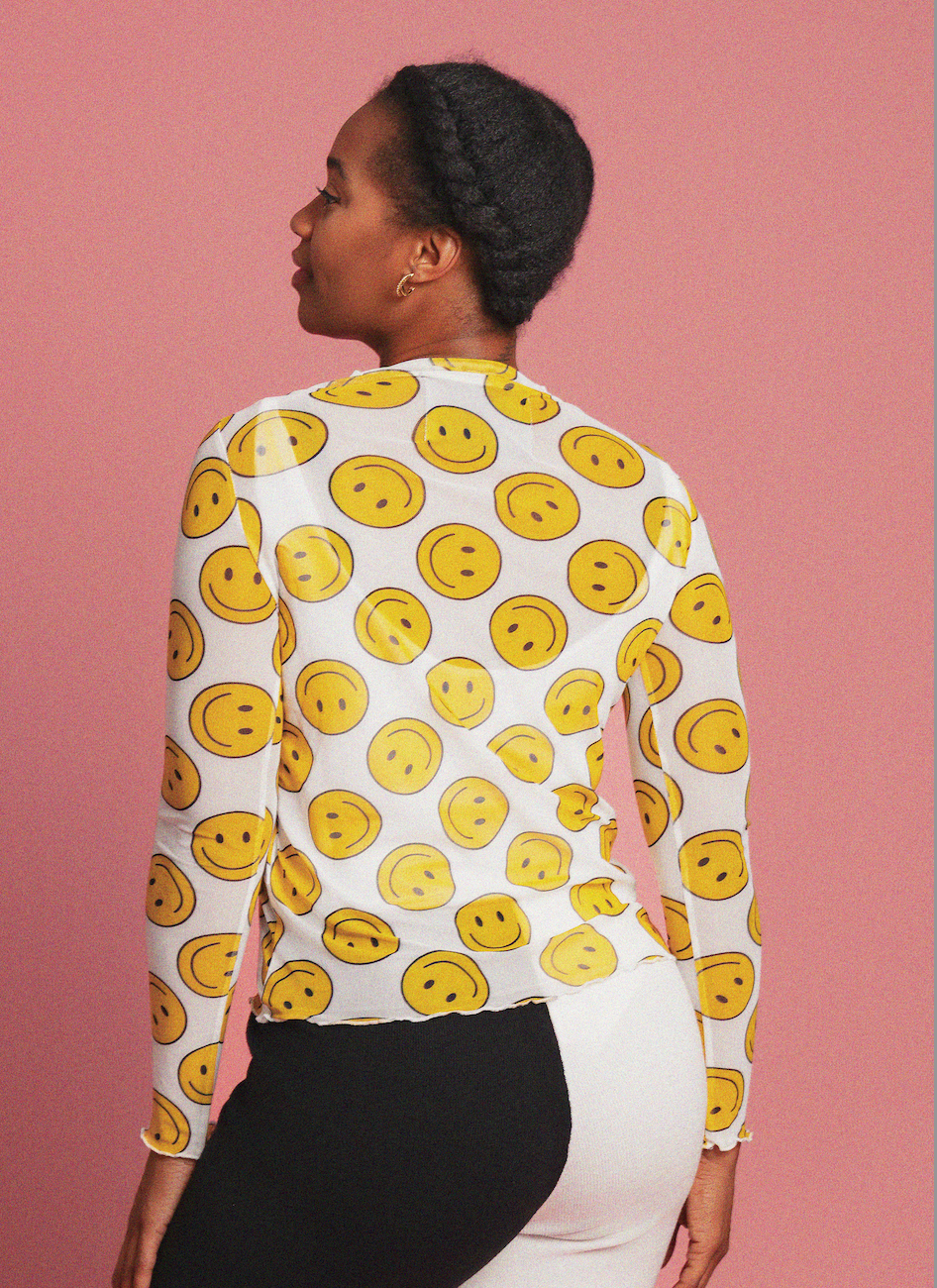 Person wearing a white long-sleeve shirt with yellow smiley face pattern against a pink background