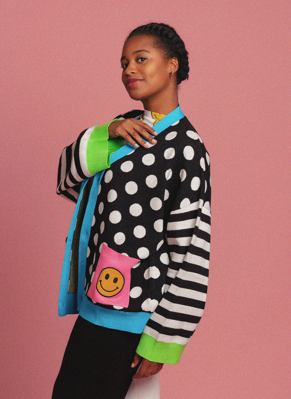 Person wearing a polka dot cardigan with smiley face designs on a pink background
