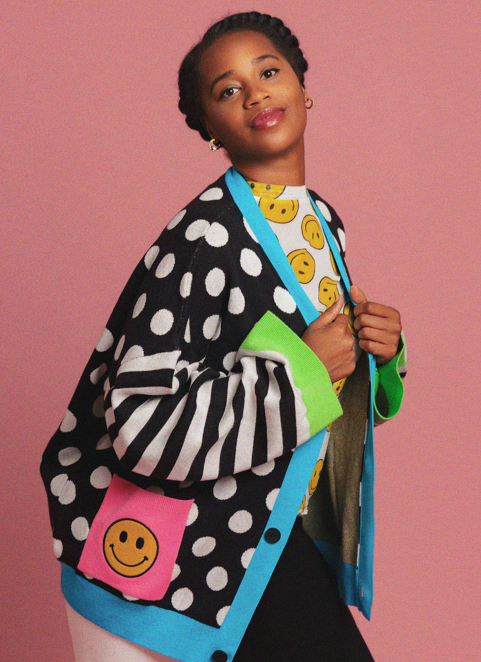 Person wearing a colorful polka dot cardigan with smiley face patterns on a pink background