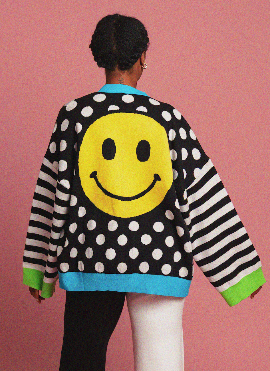 Person wearing a polka dot cardigan with smiley face designs on a pink background