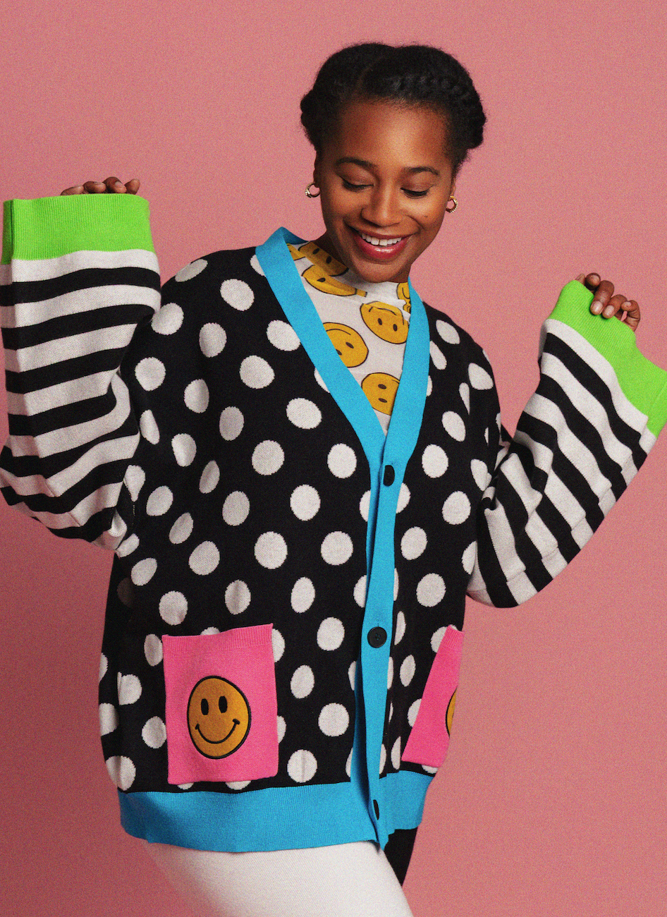 Person wearing a polka dot cardigan with smiley face designs on a pink background