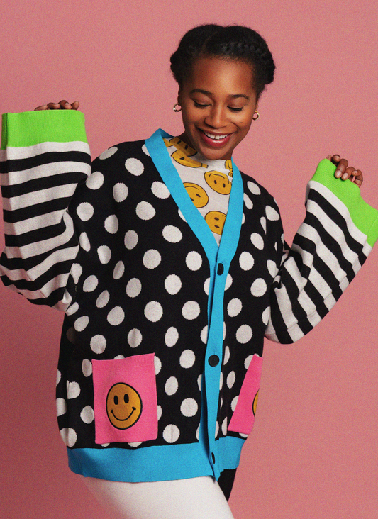 Person wearing a polka dot cardigan with smiley face designs on a pink background