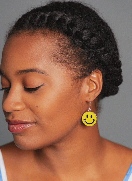 Woman wearing a yellow smiley face earring against a gray background
