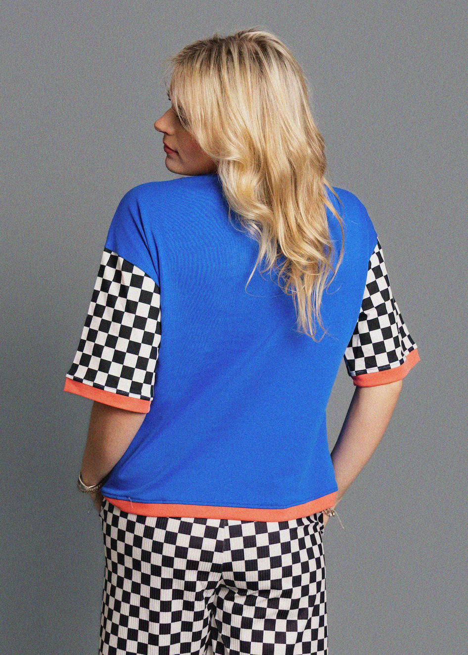 Woman wearing a blue shirt with checkered sleeves and black and white checkered pants on a gray background