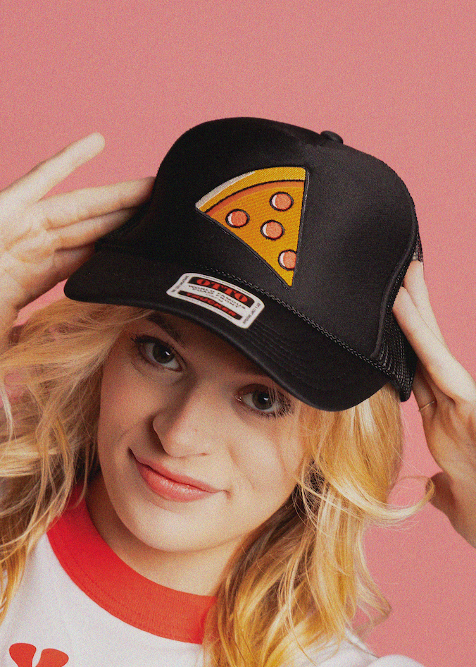 Person wearing a black cap with a pizza slice design on a pink background